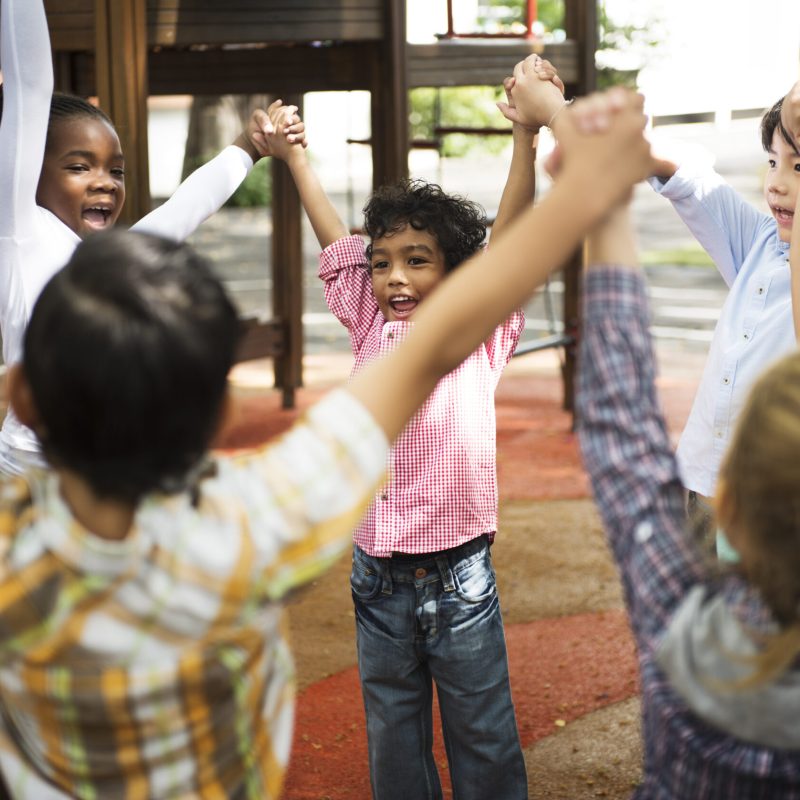 Group of diverse kindergarten students standing holding hands together