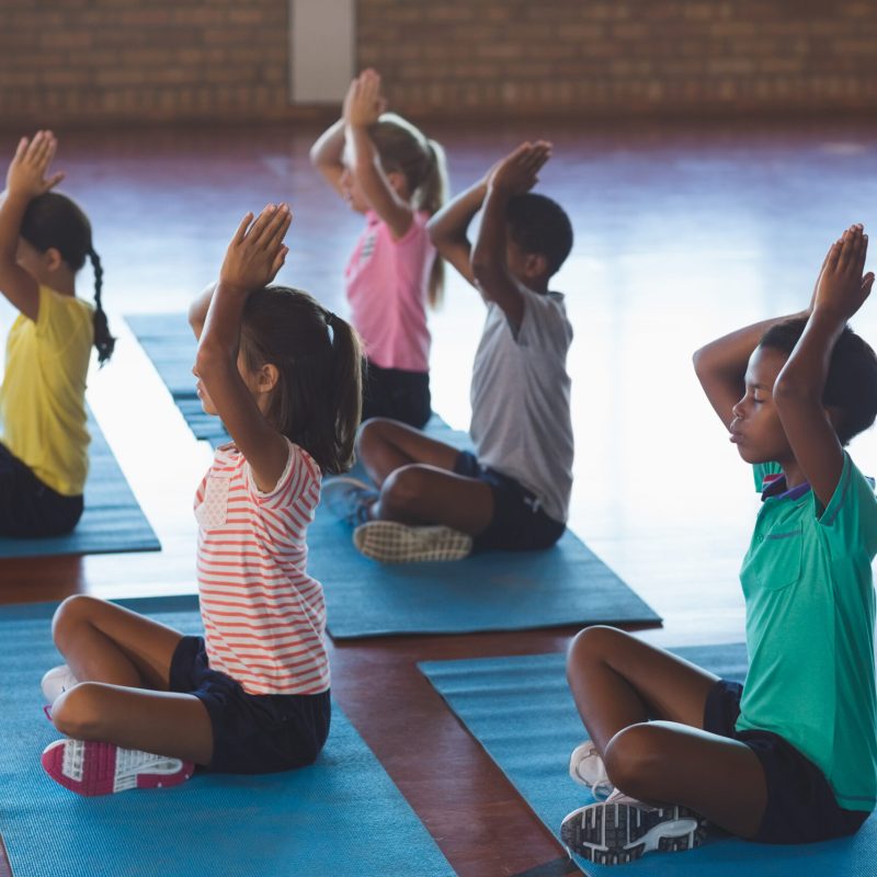 School kids meditating during yoga class in basketball court at school gym